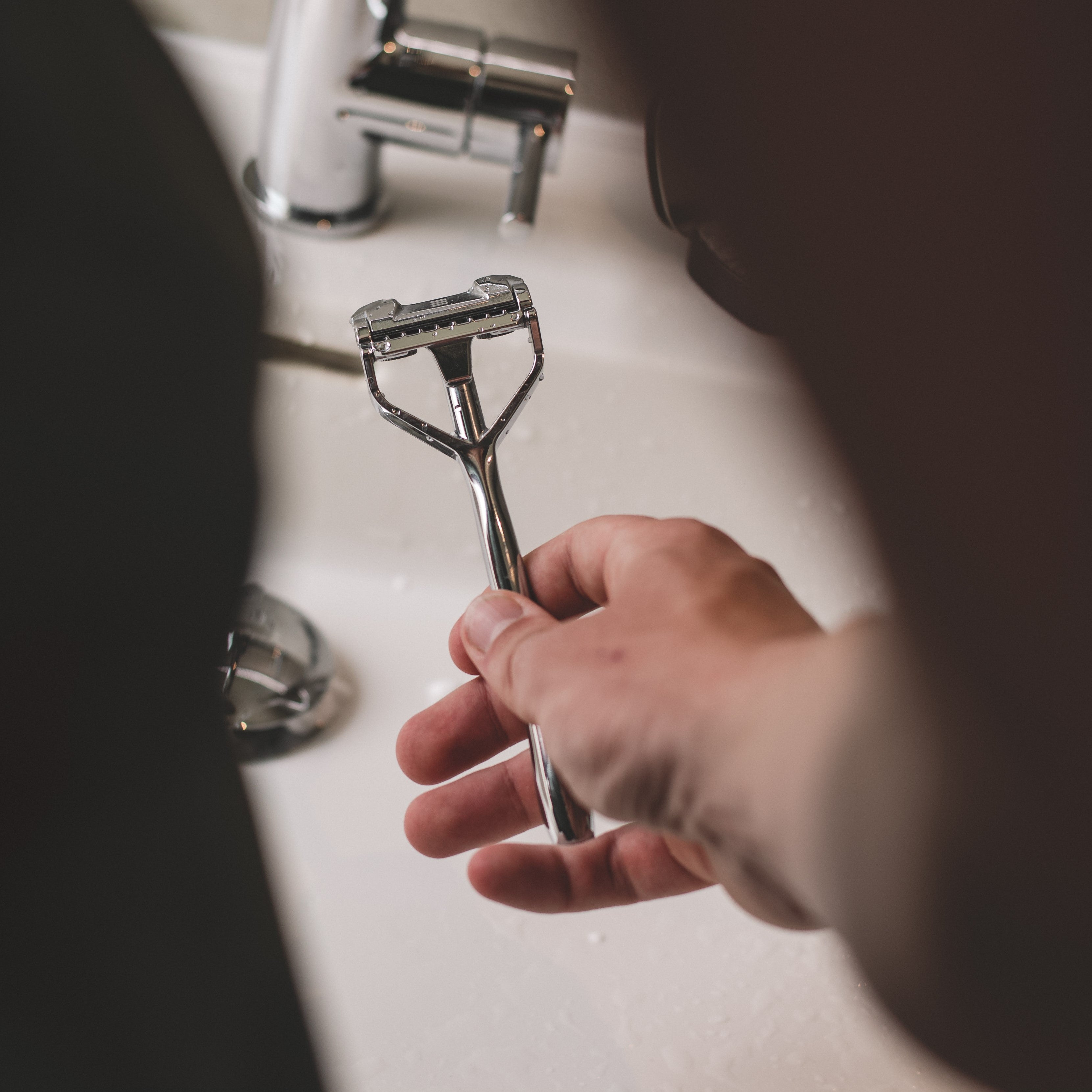 Shavent Schwingkopf Rasierer in der Hand vor einem Waschbecken