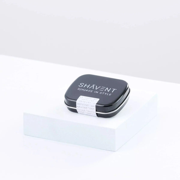 SHAVENT MĂ€nner-Geschenk-Set: Schwarze Metalldose auf Sockel, Deckel mit Logo und Slogan bedruckt, kompakter Reise-Rasierkoffer fĂŒr stilvolle Nassrasur.