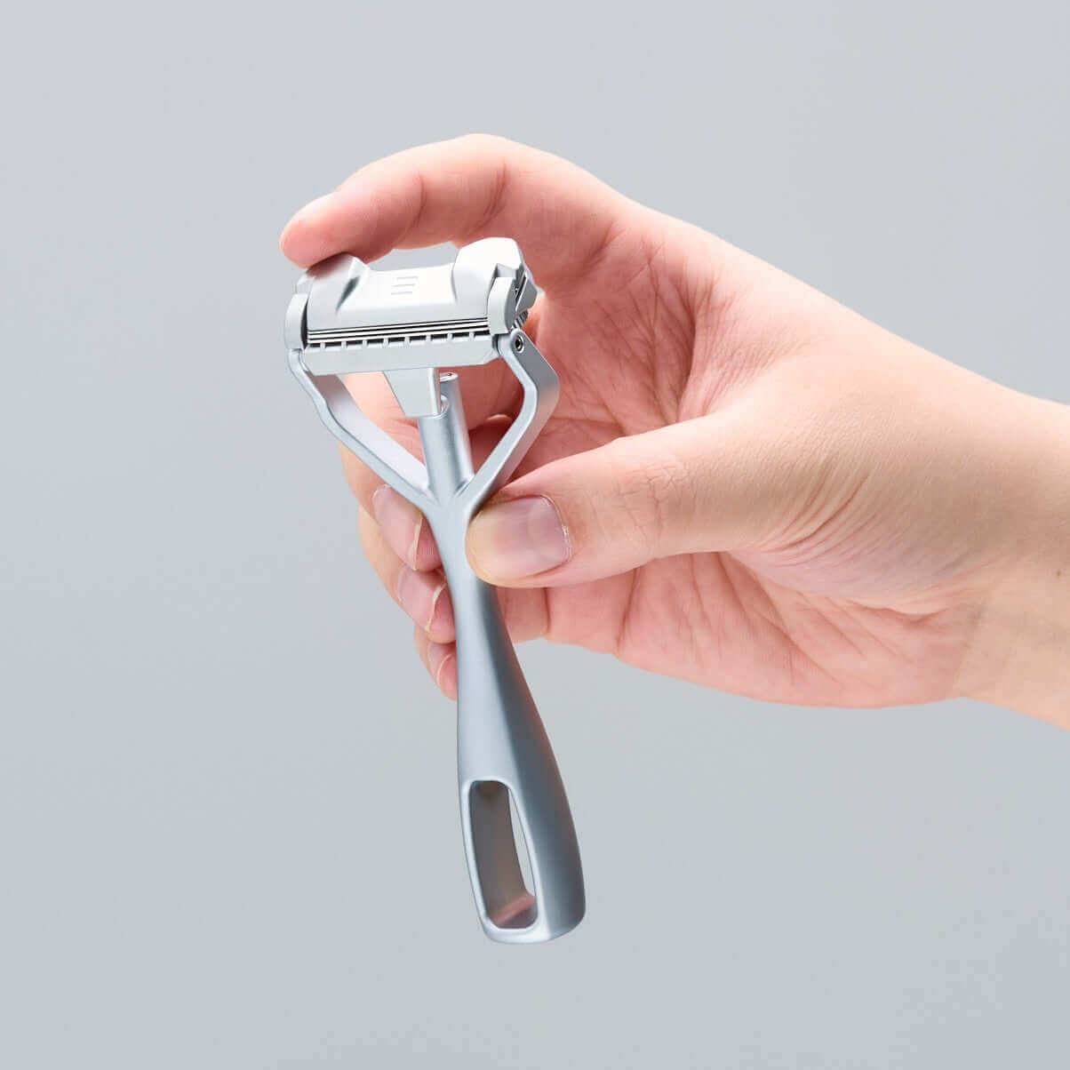 SHAVENT Compact Oster Special: Hand hält modernen Rasierer mit Metallgriff und flexiblem Kopf, ideal für sanfte Körperrasur. Enthält Kork-Klingenschutz und gratis Klingen-Test-Set.