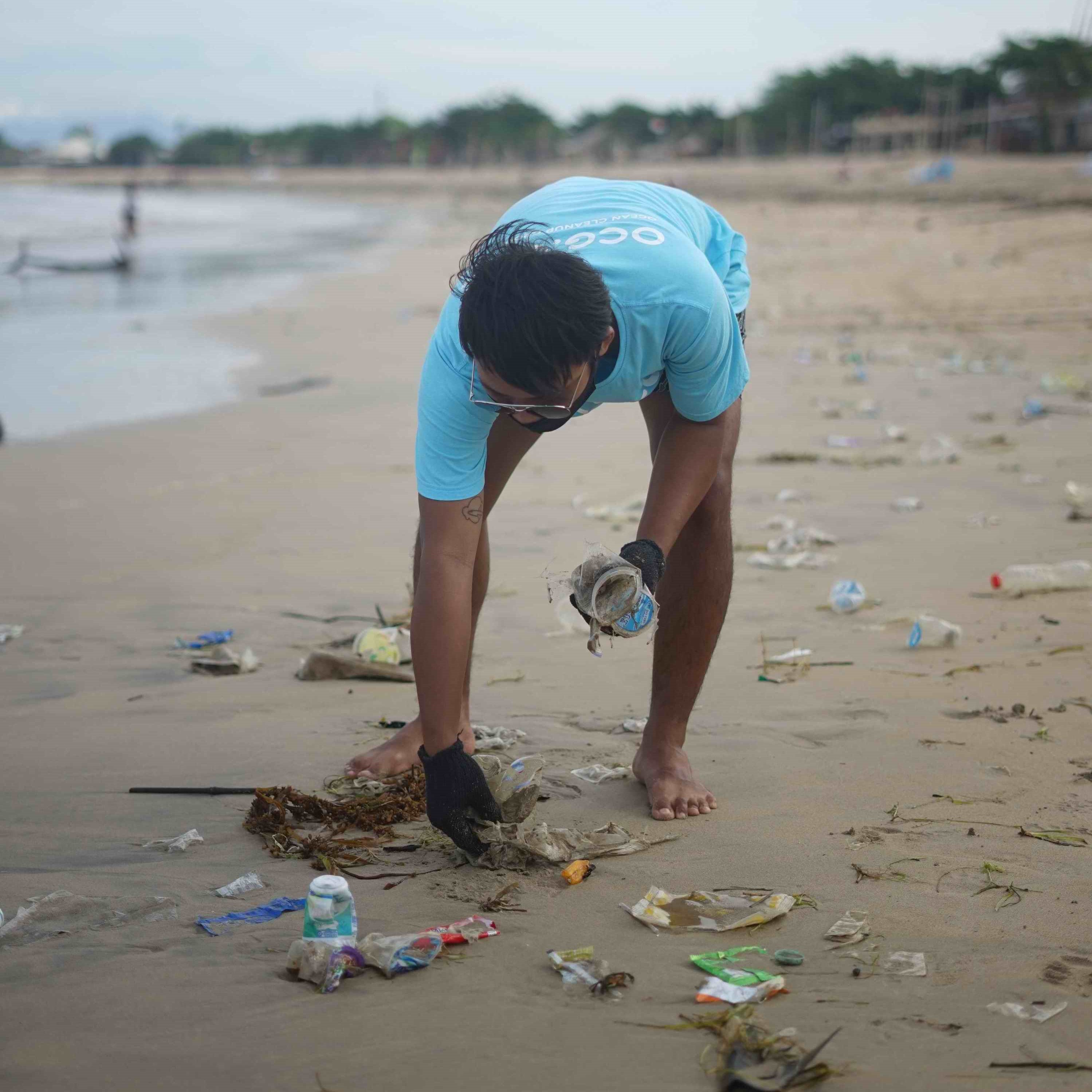 Mann sammelt Plastikmüll am Strand