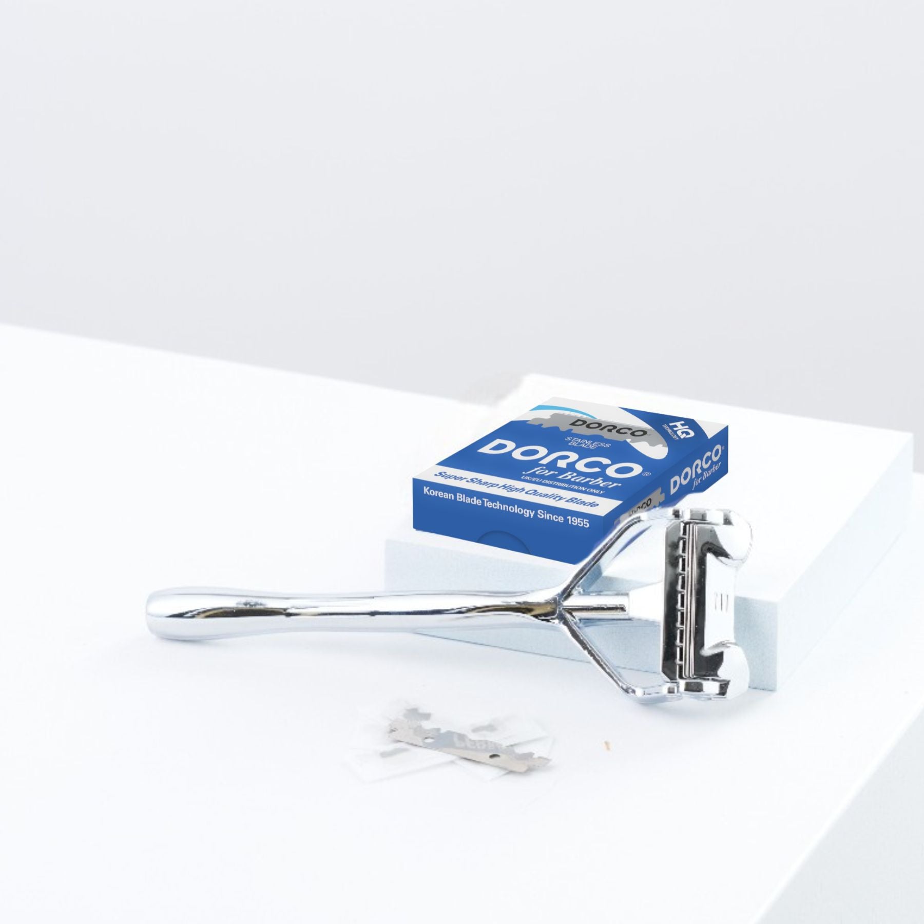 100 Rasierklingen - Dorco Blue Single Edge Halbklingen neben einem klassischen Doppelrasierer auf weißem Untergrund, mit Dorco-Box im Hintergrund. Ideal für präzise Rasuren.